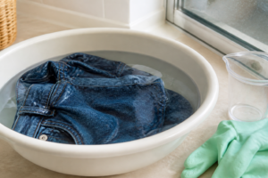 Jean en train de tremper dans une bassine pour l'éclaircir, avec gants de protection